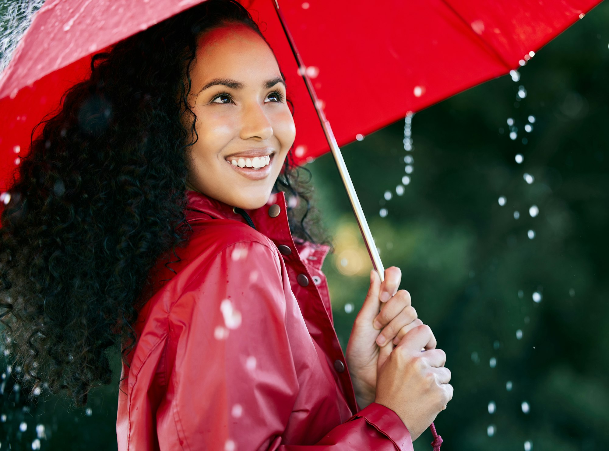 Its raining, its pouring. Shot of a beautiful young woman standing in the rain with an umbrella.